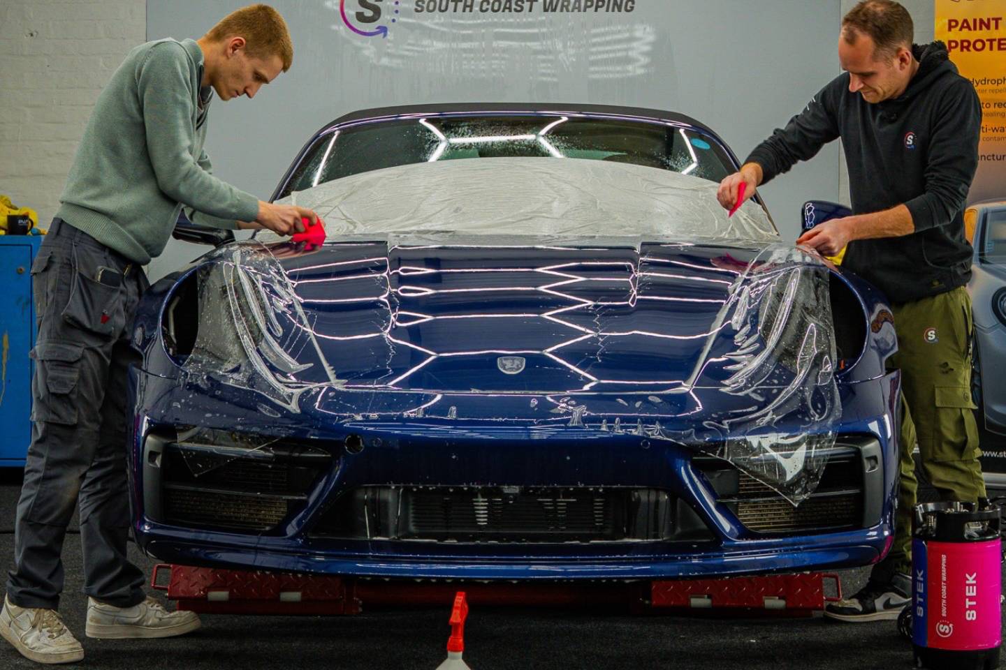 Two installers positioning paint protection film across a blue bonnet