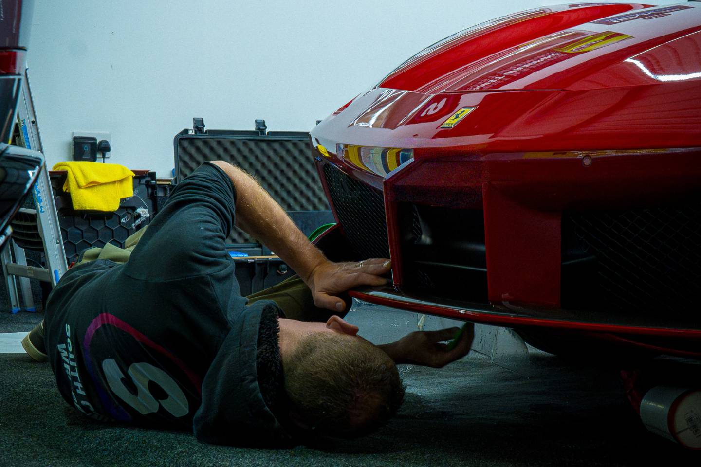 Installer working beneath the front of a red Ferrari