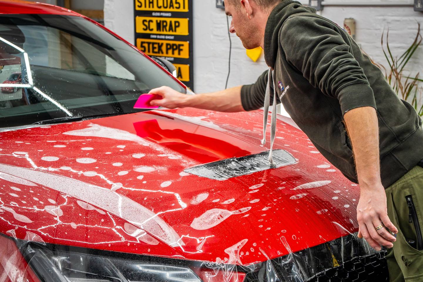 Installer smoothing paint protection film across a red bonnet