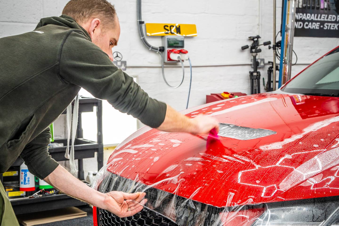 Installer positioning clear film over a red Ferrari bonnet