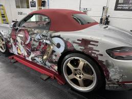 Side view of silver Porsche convertible with red and black anime graphics